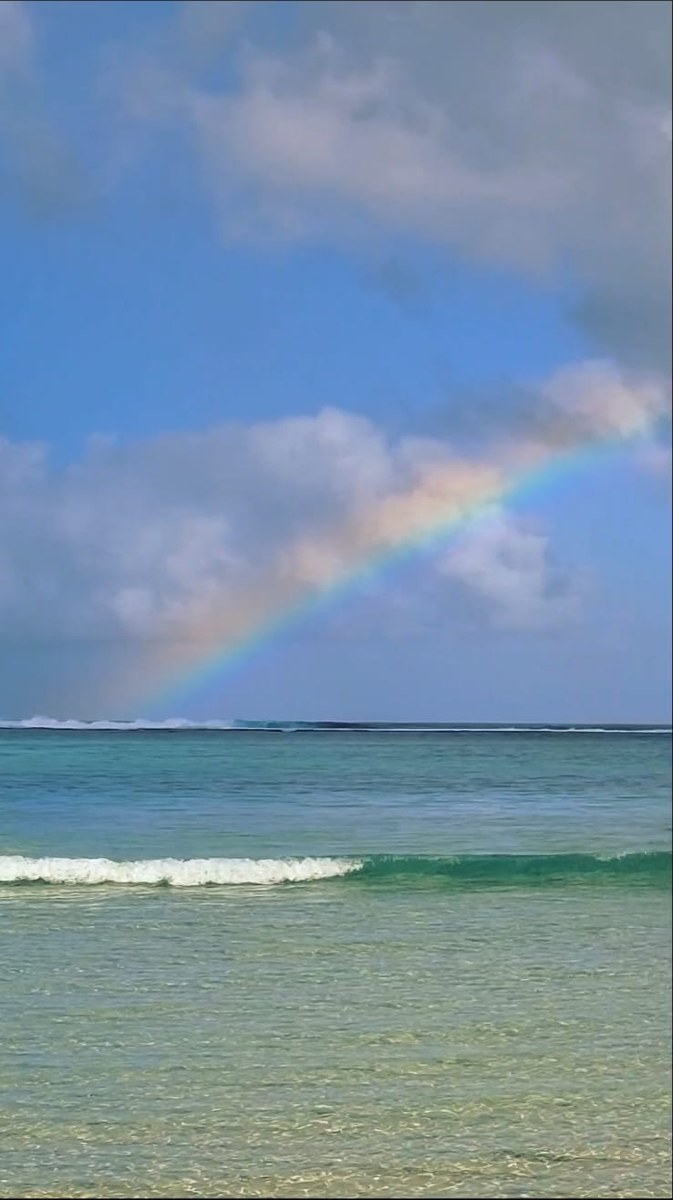 A rainbow falling into clear green water over the reef