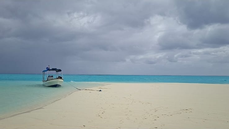 Boat on white sand and turquoise water beneath a coastal sky